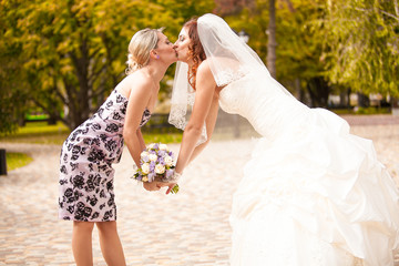 Outdoor portrait of bridesmaid kissing beautiful bride