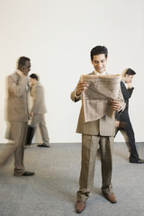 Obraz premium Businessman reading a newspaper with his colleagues in the background