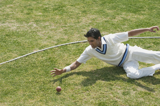 Cricket fielder diving to stop a ball near boundary line