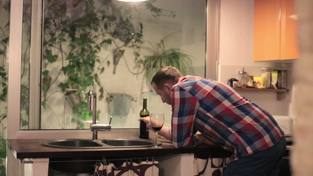 Pensive and sad young man drinking red wine in the kitchen