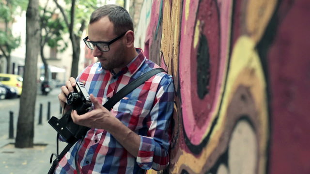 Young hipster taking photo with retro camera by graffiti wall
