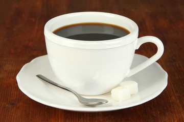 Obraz premium Hot black coffee in white ceramic cup with saucer, spoon, and sugar cubes on dark wooden table