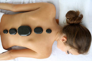 Beautiful young woman having stone massage in spa salon