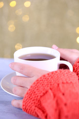 Hands holding mug of hot drink, close-up, on bright background