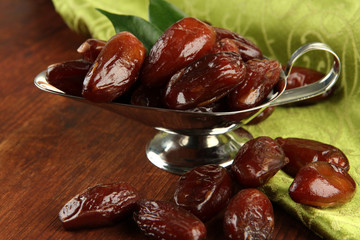 Dried dates in metal dish with napkin on wooden background