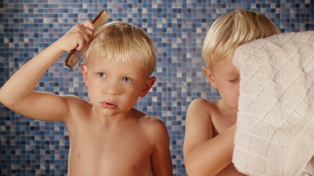 blond twin brothers combing hair drying face with towel in bathr