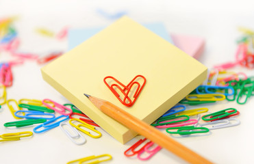 Small note pad and pencil with paper clips on white.