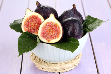 Ripe figs in bowl on wooden table close-up