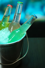 Bottled drinks in ice bucket on table on bright background