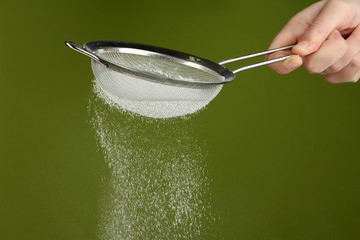 Sieve and powdered sugar on green background