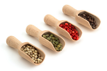 varieties of peppercorns in wooden scoops on white background