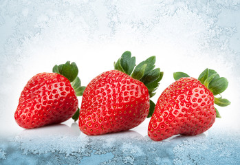 Three fresh strawberries lay on blue ice background
