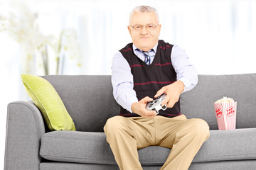 Senior man seated on a sofa playing video games at home
