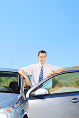 Smiling guy posing next to his car on an open road