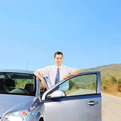 Smiling guy posing next to his automobile on an open road