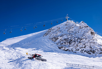 Fototapeta na wymiar Chair lift and snow groomer in Alps