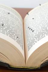 Fototapeta premium Old open book with magic falling letters on wood
