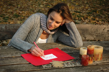 woman writing word LOVE, paper on wooden table
