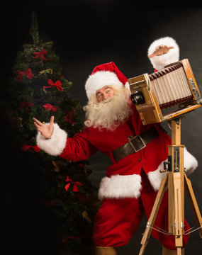 Santa Claus taking picture with old wooden camera standing near