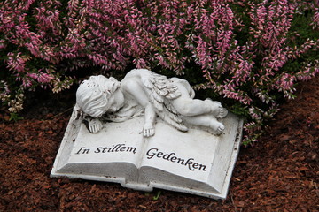 Friedhof - Ruhender Engel liegt auf Buch neben Heidekraut
