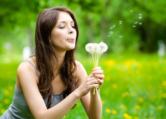 Woman blows dandelions in the park