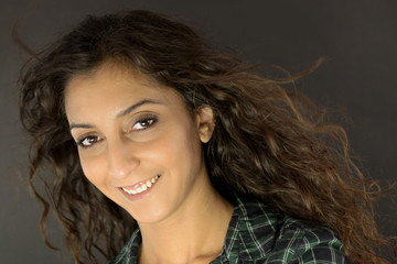 Portr&auml;t einer s&uuml;&szlig;en, charmanten und h&uuml;bschen Frau mit lockigem, br&uuml;nettem Haar, das im Wind weht. Sie l&auml;chelt wie in einem Musikvideo, w&auml;hrend ihre langen Haare vom Wind getragen werden.