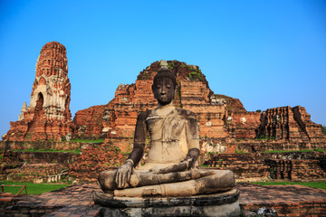 ancient big Buddha statue in front of damaged brick pagoda on bl