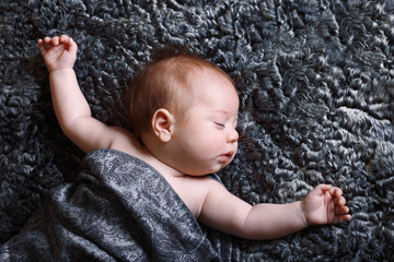 baby sleeps arms outstretched on gray astrakhan