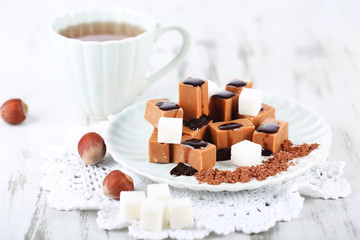 Many toffee on plate and cup of tea on napkin on wooden table
