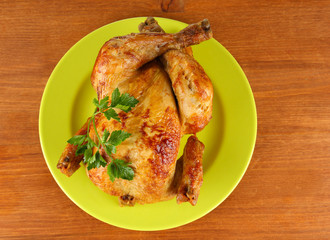 Roasted whole chicken on a green plate on wooden background