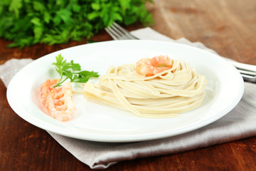 Pasta with shrimps on white plate, on wooden background