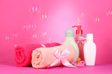 Baby cosmetics and towels on pink background