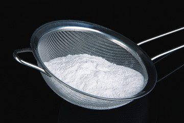 Powdered sugar in metal sieve on black background