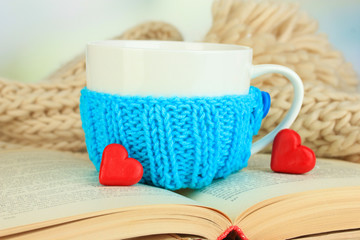 Fototapeta na wymiar Cup with knitted thing on it and open book close up