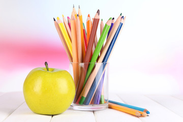 Colorful pencils in glass on wooden table on bright background