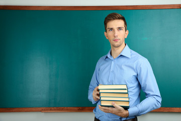 Young teacher with books near chalkboard in school classroom