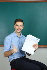 Young teacher sitting near chalkboard in school classroom