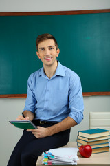 Young teacher sitting on desk in school classroom