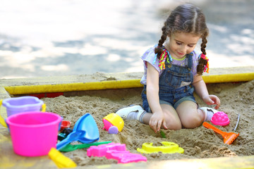 Little girl sitting in sandbox and playing with molds