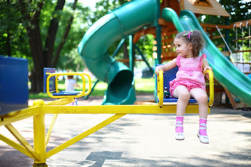 Fototapeta na wymiar Little girl in dress on carousel spins on playground