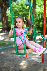 Little girl in pink dress sitting on swing at playground