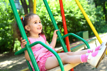 little girl in dress swinging on a swing at playground