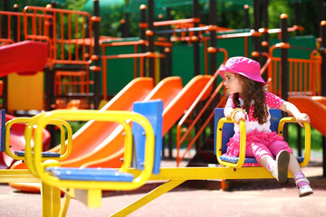 Fototapeta na wymiar Serious little girl in a pink hat whirls on the carousel