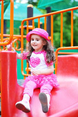 Fototapeta na wymiar Smiling little girl rolling down the hill on playground