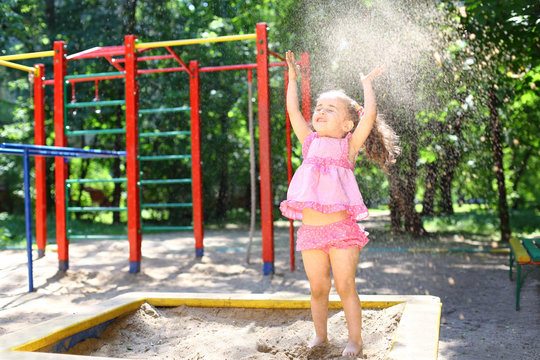 A little girl cheerfully throws up sand in the sandbox