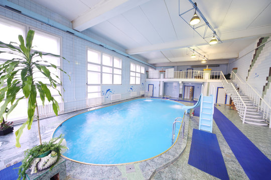 Empty oval indoor swimming pool with a small slide