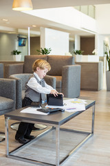 little boy in tie with stationery on table in business center