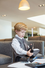 little boy in tie leafs through notebook in business center