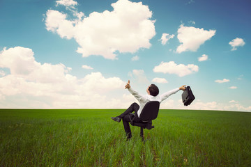 businessman in a field with a blue sky sitting on an office chai