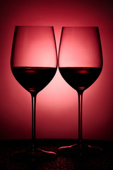 Two glasses filled with red wine against red background
